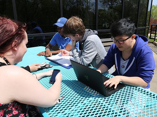 户外学生学习与计算机和笔记本在明亮的蓝色野餐桌上。